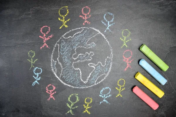 On a dark stone surface, a globe was painted with chalk and different-colored male figures drawn on the outside - concept of diversity and tolerance represented worldwide by a chalk drawing