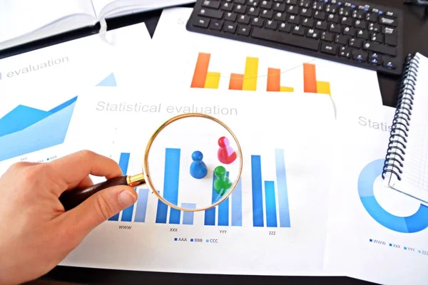 Genç bir adam, istatistik rakamları bakarak, elinde bir büyüteç tutuyor-örnekleme ve doğru hedef grubu seçerek ve onu inceleyerek konu üzerinde bir iş kavramı 