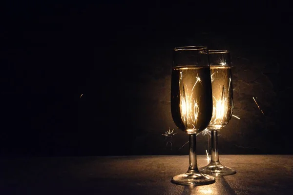 两个充满香槟的长笛站在黑暗中的火花 照亮他们与火花从后面 概念的新年前夜和烟花的空间文本和其他对象 — 图库照片