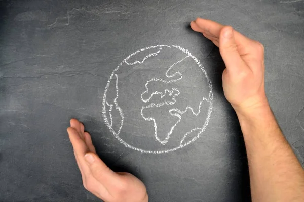 On a dark stone surface, a globe was painted with chalk and different-colored male figures drawn on the outside - concept of diversity and tolerance represented worldwide by a chalk drawing