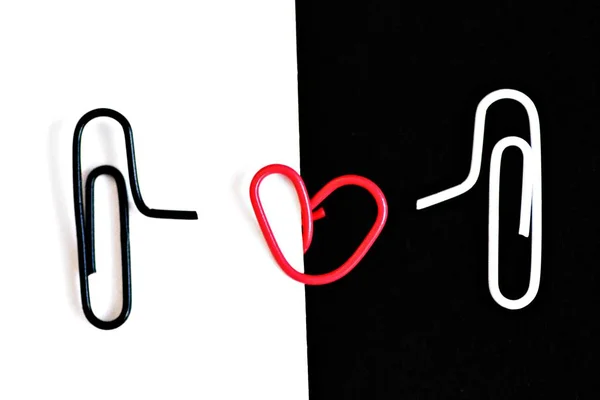 白色剪切的回形针位于黑色表面上 另一个黑色回形针位于白色地板上 中间有一个红色的回形针弯曲成心 一个带有回形针的爱的概念 — 图库照片