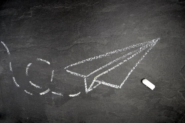 With a chalk drawn a paper plane and a dashed way on a dark marble surface - background with a flying paper plane