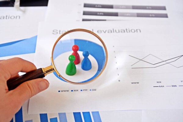 Молодой человек держит увеличительное стекло в руке, рассматривая статистические данные - бизнес-концепцию на тему отбора проб и выбора правильной целевой группы и изучения ее
 