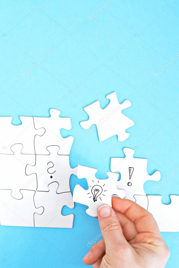 There are puzzle pieces on one face, one on a question mark, the other on an exclamation mark. A hand connects these two parts with a light bulb puzzle piece. Concept for generating ideas with space 