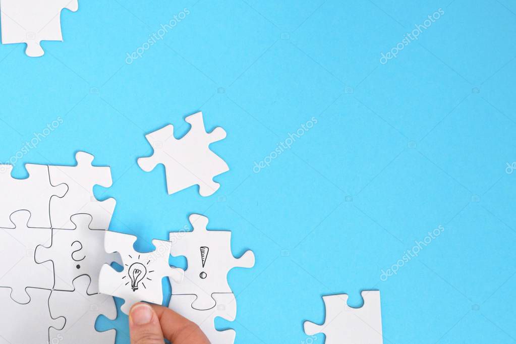There are puzzle pieces on one face, one on a question mark, the other on an exclamation mark. A hand connects these two parts with a light bulb puzzle piece. Concept for generating ideas with space 