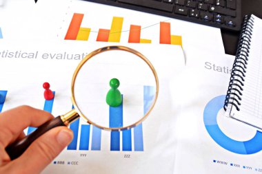 Genç bir adam, istatistik rakamları bakarak, elinde bir büyüteç tutuyor-örnekleme ve doğru hedef grubu seçerek ve onu inceleyerek konu üzerinde bir iş kavramı 