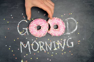 Tebeşir karanlık bir taş yüzeye yazıldı. Günaydın, O kelimeden O kelime beyaz Sprinkles ile iki pembe donut ile değiştirildi-tatlı donut ile güne mutlu başlangıç