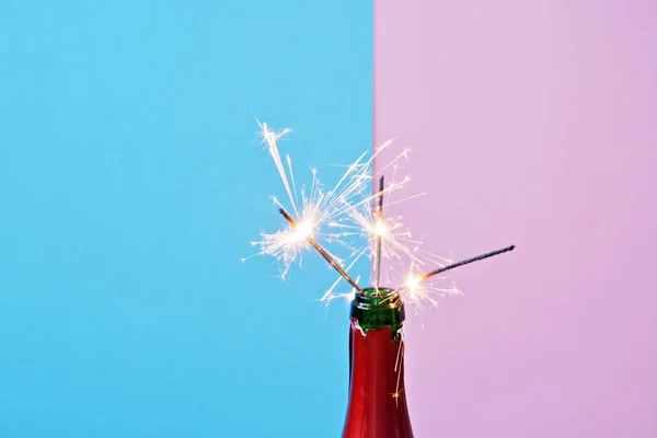 A empty champagne bottle in the neck of which a few sparklers are glowing - two toned background with a bottle of champagne in front of it and sparkles in it