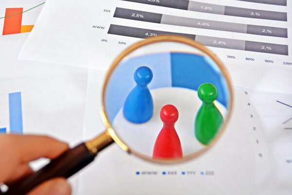 Молодой человек держит увеличительное стекло в руке, рассматривая статистические данные - бизнес-концепцию на тему отбора проб и выбора правильной целевой группы и изучения ее
 