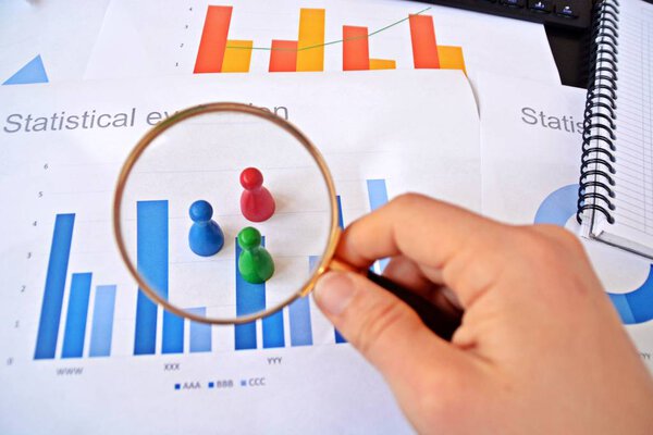 A young man is holding a magnifying glass in his hand, looking at statistic figures - a business concept on the subject of sampling and selecting the right target group and examining it 