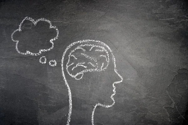 The silhouette of a head drawn with chalk on a dark stone surface as a concept and symbol for the thought process and the brainstorming for the unfolding of creativity and problem solving