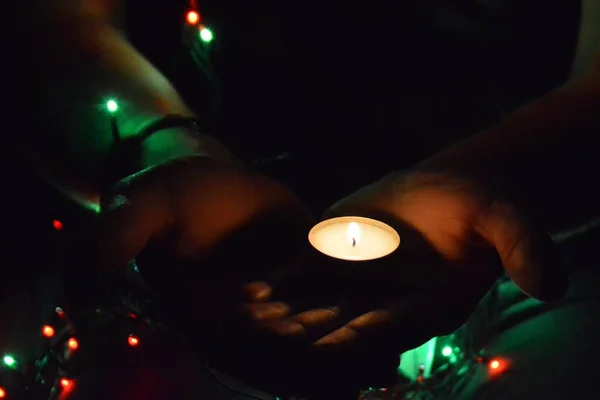 A man in his twenties holding a burning tealight in his hands, in the background are various colored LED lights to see - contemplative Christmas Eve with a small candle and colorful lights