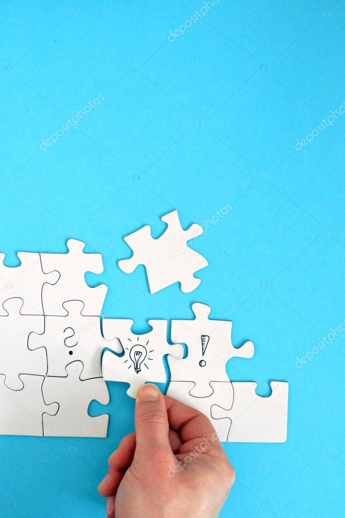 There are puzzle pieces on one face, one on a question mark, the other on an exclamation mark. A hand connects these two parts with a light bulb puzzle piece. Concept for generating ideas with space 