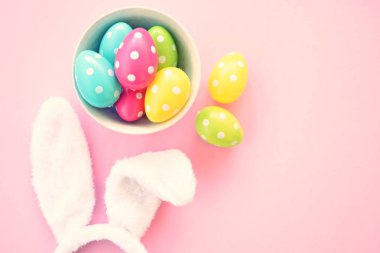 Üzerinde tavşan kulakları olan bir saç bandı pembe bir arka plan üzerinde, yanında beyaz noktalı Paskalya yumurtaları dolu bir eşarp - pastel renkleri ile Paskalya için renkler ile kavram -
