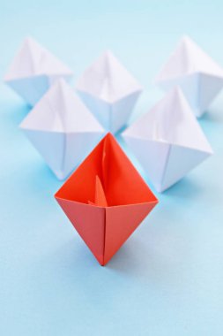 Kırmızı kendi kendine katlanmış kağıt tekne mavi bir yüzey üzerinde yatıyor, birçok beyaz tekneler izledi-kavramı liderlik sembolize