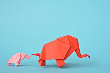 Mavi bir arka plan üzerinde pembe ve kırmızı stand iki kağıt katlanmış filler - küçük bir bebek fil ve origami tekniğine göre katlanmış bir anne fil ile kavram
