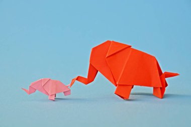 Küçük ve büyük bir origami fil iki fil gibi görünen bir ayna parçası önünde tek renkli bir yüzey üzerinde kırmızı ve pembe kağıt standı katlanmış bir su deliğinin önünde duruyor 