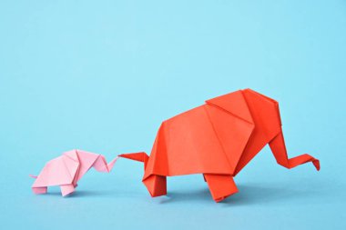 Mavi bir arka plan üzerinde pembe ve kırmızı stand iki kağıt katlanmış filler - küçük bir bebek fil ve origami tekniğine göre katlanmış bir anne fil ile kavram