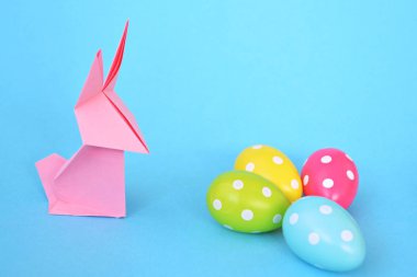 Pastel kağıt tan katlanmış pembe bir origami tavşan ı da beyaz nokta ile Paskalya yumurtası olan mavi bir taban üzerinde duruyor - origami ve metin veya Paskalya için diğer unsurlar için alan kavramı 