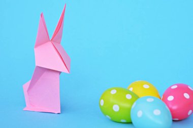 Pastel kağıt tan katlanmış pembe bir origami tavşan ı da beyaz nokta ile Paskalya yumurtası olan mavi bir taban üzerinde duruyor - origami ve metin veya Paskalya için diğer unsurlar için alan kavramı 