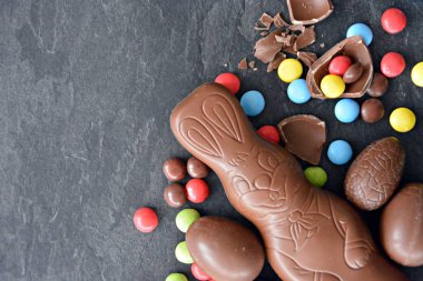 Bir çikolata paskalya tavşanı renkli çikolata parçaları ve birkaç çikolata yumurta ile koyu mermer bir yüzey üzerinde yatıyor - metin veya diğer unsurlar için oda ile paskalya için tatlılar ile kavram 