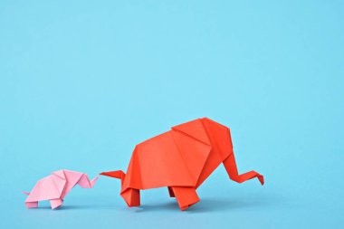 Mavi bir arka plan üzerinde pembe ve kırmızı stand iki kağıt katlanmış filler - küçük bir bebek fil ve origami tekniğine göre katlanmış bir anne fil ile kavram