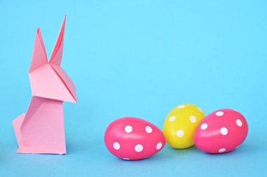 Pastel kağıt tan katlanmış pembe bir origami tavşan ı da beyaz nokta ile Paskalya yumurtası olan mavi bir taban üzerinde duruyor - origami ve metin veya Paskalya için diğer unsurlar için alan kavramı 