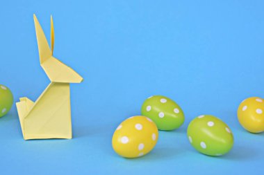 Pastel kağıt tan katlanmış pembe bir origami tavşan ı da beyaz nokta ile Paskalya yumurtası olan mavi bir taban üzerinde duruyor - origami ve metin veya Paskalya için diğer unsurlar için alan kavramı 