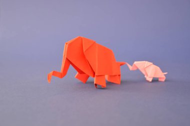 Küçük ve büyük bir origami fil iki fil gibi görünen bir ayna parçası önünde tek renkli bir yüzey üzerinde kırmızı ve pembe kağıt standı katlanmış bir su deliğinin önünde duruyor 