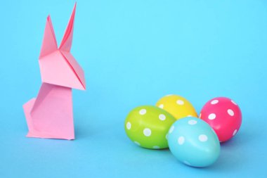 Pastel kağıt tan katlanmış pembe bir origami tavşan ı da beyaz nokta ile Paskalya yumurtası olan mavi bir taban üzerinde duruyor - origami ve metin veya Paskalya için diğer unsurlar için alan kavramı 