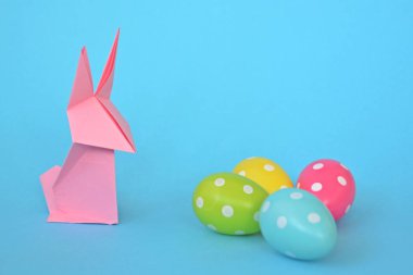 Pastel kağıt tan katlanmış pembe bir origami tavşan ı da beyaz nokta ile Paskalya yumurtası olan mavi bir taban üzerinde duruyor - origami ve metin veya Paskalya için diğer unsurlar için alan kavramı 