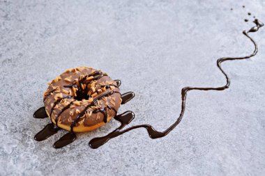 Çikolata sır ve karamel slivers ile bir donut gri mermer yüzeyinde yatıyor ve çikolata sosu ile üzerine dökülür