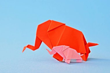 Küçük ve büyük bir origami fil iki fil gibi görünen bir ayna parçası önünde tek renkli bir yüzey üzerinde kırmızı ve pembe kağıt standı katlanmış bir su deliğinin önünde duruyor 