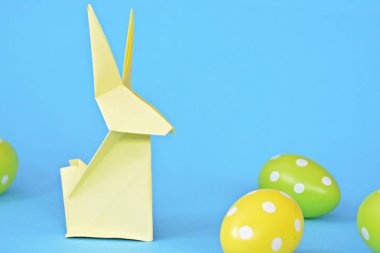 Pastel kağıt tan katlanmış pembe bir origami tavşan ı da beyaz nokta ile Paskalya yumurtası olan mavi bir taban üzerinde duruyor - origami ve metin veya Paskalya için diğer unsurlar için alan kavramı 