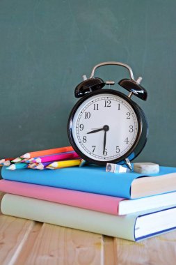 Bir çalar saat renkli kitaplar ve yeşil elma ile bir tahta önünde duruyor - ilköğretim okulunda okul ve zaman yönetimi konusunda metin veya diğer unsurlar için alan ile kavram
