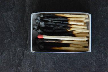 arka plan üzerinde son bir yanmamış eşleşme ile kibrit kutusunda birçok yanmış eşleşmelerin yakın çekim görünümü