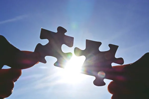 A person holds two puzzle pieces in his hand that fit together, in the background the sun shines and illuminates the parts from behind - concept for brainstorming in the professional environment