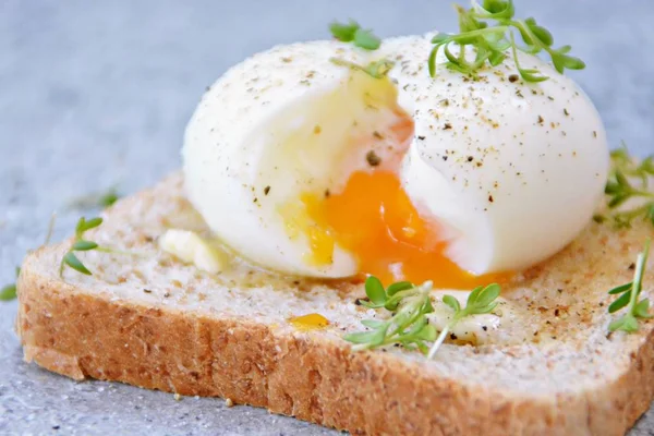 On a freshly roasted whole wheat toast is a boiled egg with soft egg yolk, which flows out of the egg. On the egg is cress and salt and pepper