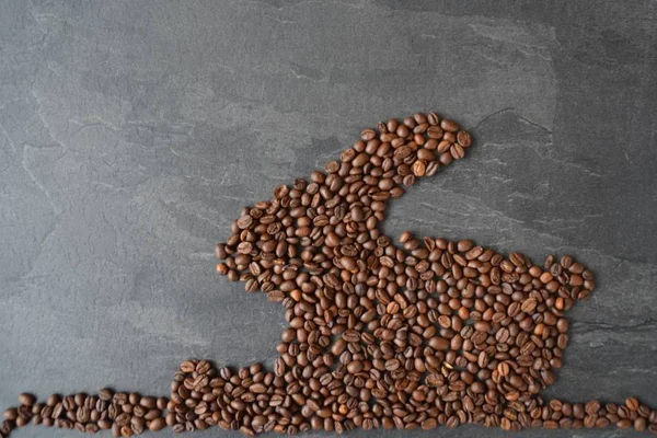 An Easter bunny made of freshly roasted coffee beans laid out with a cup of coffee - concept for fresh coffee enjoyment on easter and as easter gift in the form of coffee beans