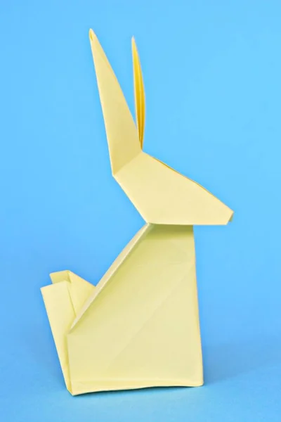 パステルペーパーから折りたたまれた折り紙のウサギは 青いベースに立っています 折り紙とイースターのためのテキストや他の要素のための場所との概念 — ストック写真