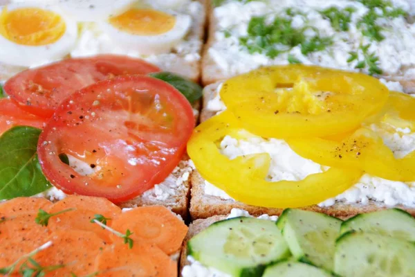 Many whole-grain toasts with different toppings lie on a dark surface - concept for healthy nutrition with vegetables on a wholemeal toast and coarse-grained cream cheese as background