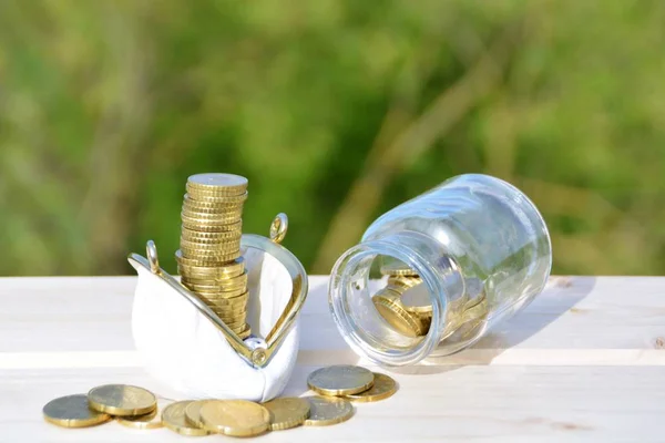 A jar full of savings stands on a space next to a purse of saved coins that pile up to form a tall tower - saving concept with room for text or other items