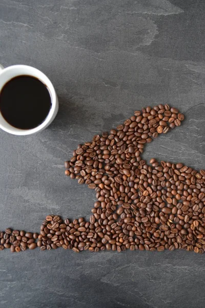 An Easter bunny made of freshly roasted coffee beans laid out with a cup of coffee - concept for fresh coffee enjoyment on easter and as easter gift in the form of coffee beans