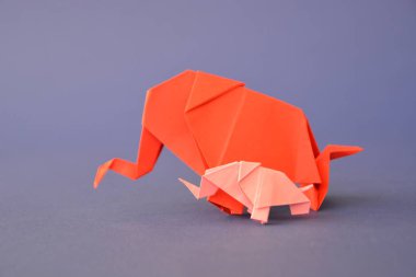 Küçük ve büyük bir origami fil iki fil gibi görünen bir ayna parçası önünde tek renkli bir yüzey üzerinde kırmızı ve pembe kağıt standı katlanmış bir su deliğinin önünde duruyor 