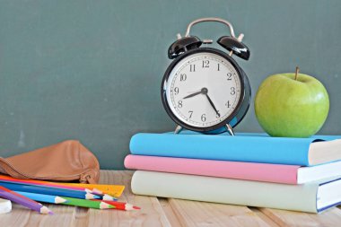 Bir çalar saat renkli kitaplar ve yeşil elma ile bir tahta önünde duruyor - ilköğretim okulunda okul ve zaman yönetimi konusunda metin veya diğer unsurlar için alan ile kavram
