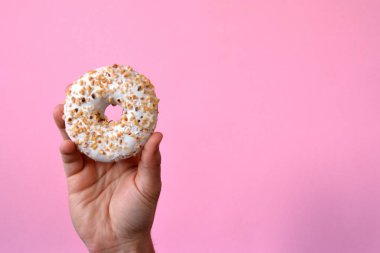 Bir el Çikolata buzlanma ile bir donut tutar yukarı. Arka plan renkli ve metin veya diğer unsurlar için oda bırakır