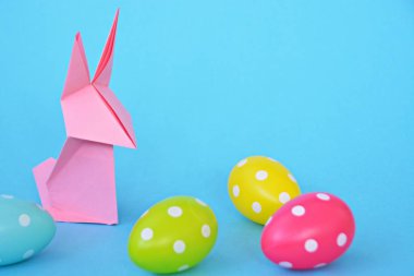 Pastel kağıt tan katlanmış pembe bir origami tavşan ı da beyaz nokta ile Paskalya yumurtası olan mavi bir taban üzerinde duruyor - origami ve metin veya Paskalya için diğer unsurlar için alan kavramı 