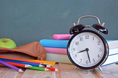 Bir çalar saat renkli kitaplar ve yeşil elma ile bir tahta önünde duruyor - ilköğretim okulunda okul ve zaman yönetimi konusunda metin veya diğer unsurlar için alan ile kavram