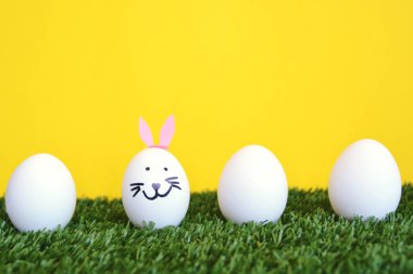 bir tavşan yüzü ile boyanmış ve tavşan kulakları yapıştırılmış yumurta metin veya diğer öğeler için alan ile ahşap bir arka plan önünde bir çim alan üzerinde yalan