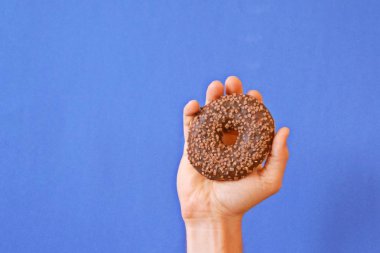 Bir el Çikolata buzlanma ile bir donut tutar yukarı. Arka plan renkli ve metin veya diğer unsurlar için oda bırakır